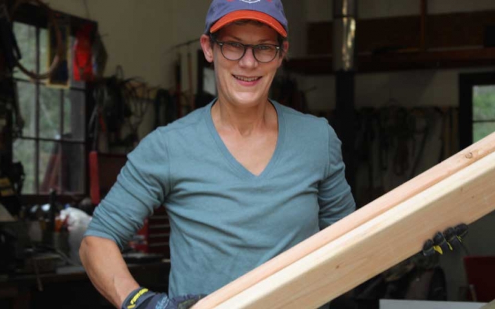 A person smiles at the camera while holding a piece of wood during a service project with Outward Bound.